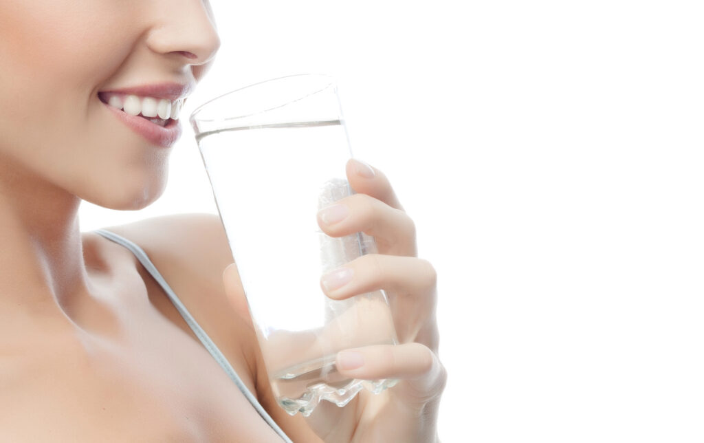 Woman with healthy white teeth drinking fluorinated water. 